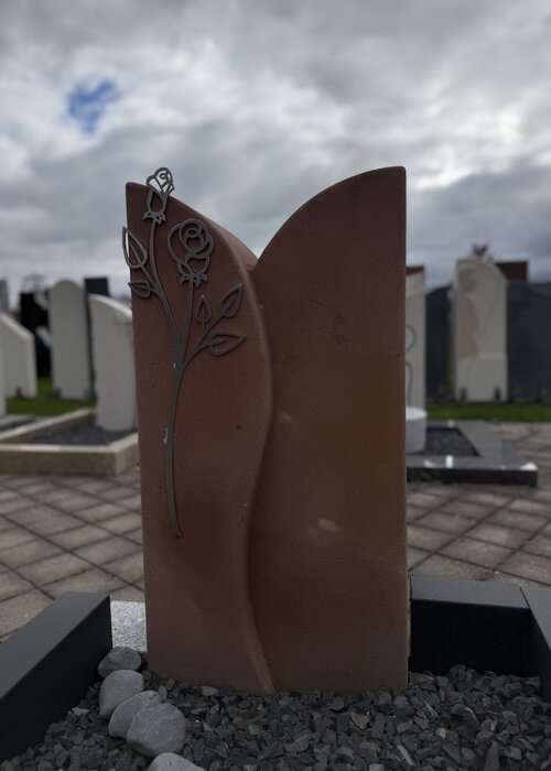 Grabstein für eine Urnengrabstelle. Das Modell heißt Los Altos. Hier ist es aus rötlichem Sandstein angefertigt. Eine Rose aus Edelstahl angebracht an der Front schmückt den Grabstein. | © Messerschmidt GmbH