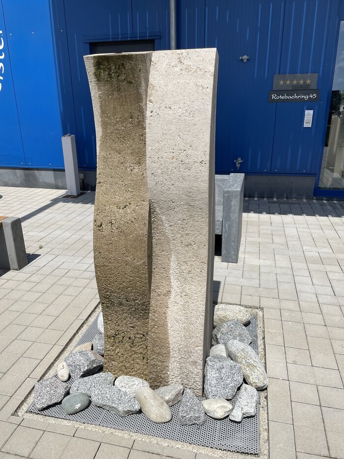 Wasser fließt einen Brunnen aus Muschelkalkstein hinunter.